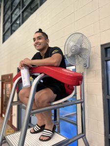 male lifeguard sitting on guard station with red floatation Device on lap