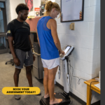 A male trainer is doing a body scan of a female client.